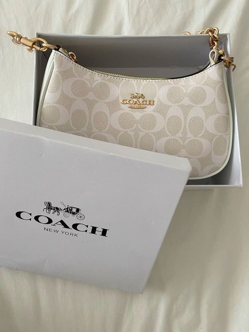 Coach handbag with gold chain and matching pouch on a light background
